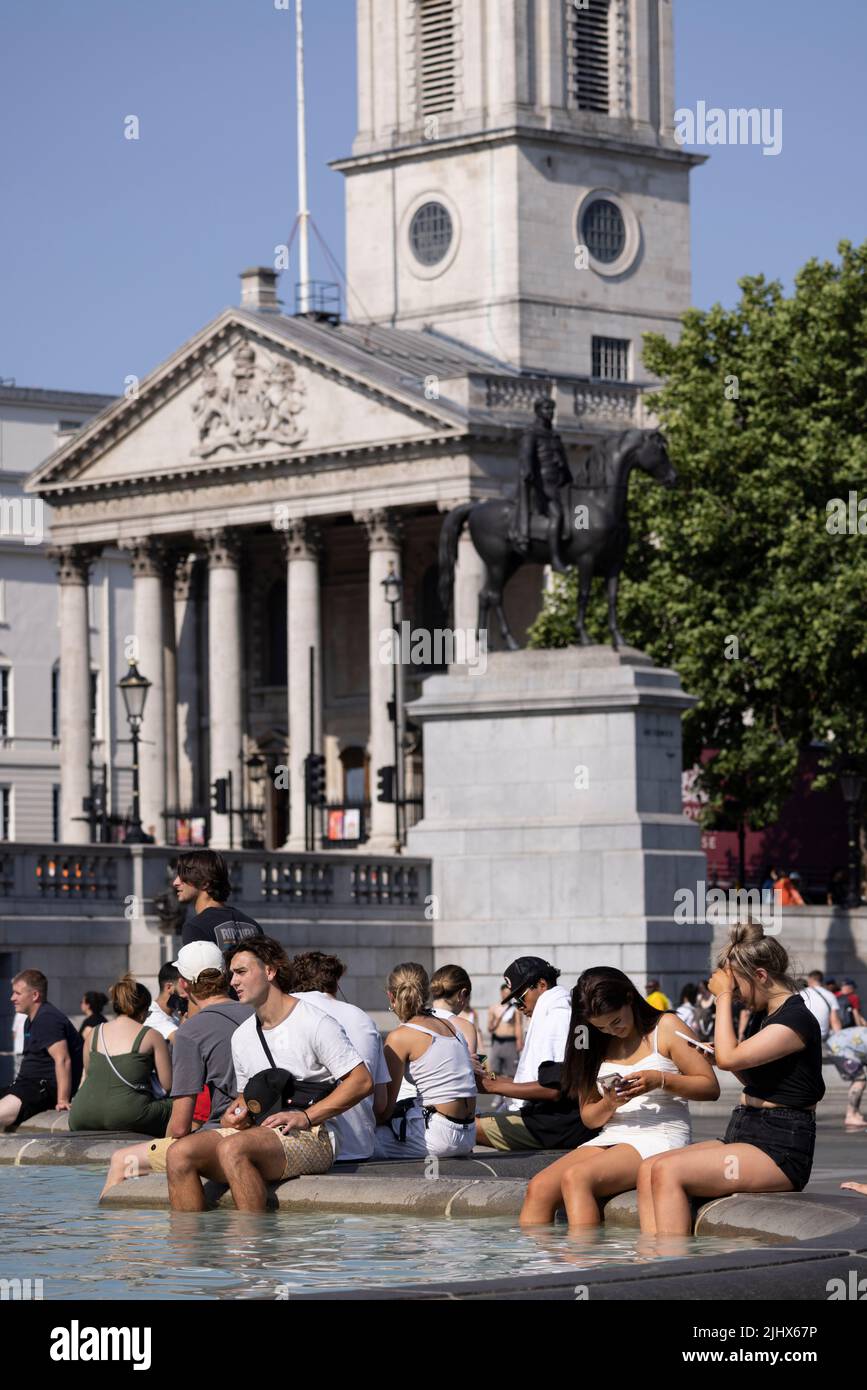 An einem der heißesten Tage in Großbritannien im Sommer, dem 2022. Juli, sitzen sich die Menschen mit ihren Beinen in den Springbrunnen am Trafalgar Square abkühlen. Stockfoto