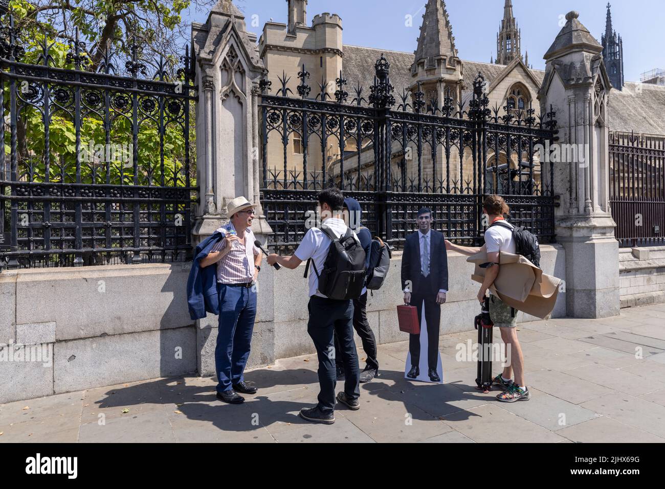 Journalisten interviewen einen Fußgänger auf der Straße vor dem Parlamentsgebäude, während sie einen großen Rishi Sunak aus Pappe, London, Großbritannien, mit sich führen Stockfoto