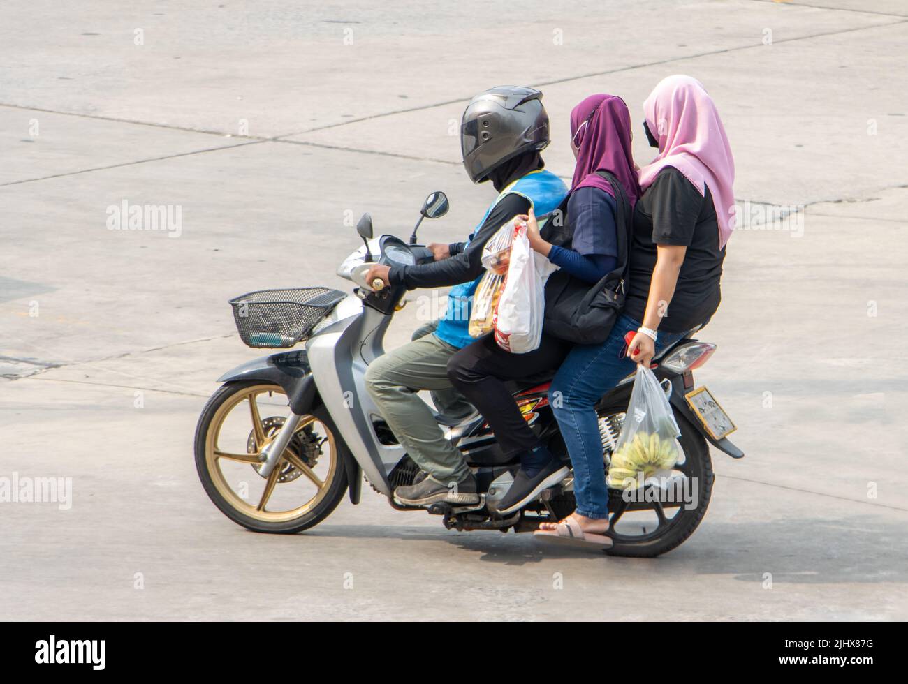 Ein Taxifahrer auf einem Motorrad fährt mit einer zwei Frau im Hijab. Stockfoto