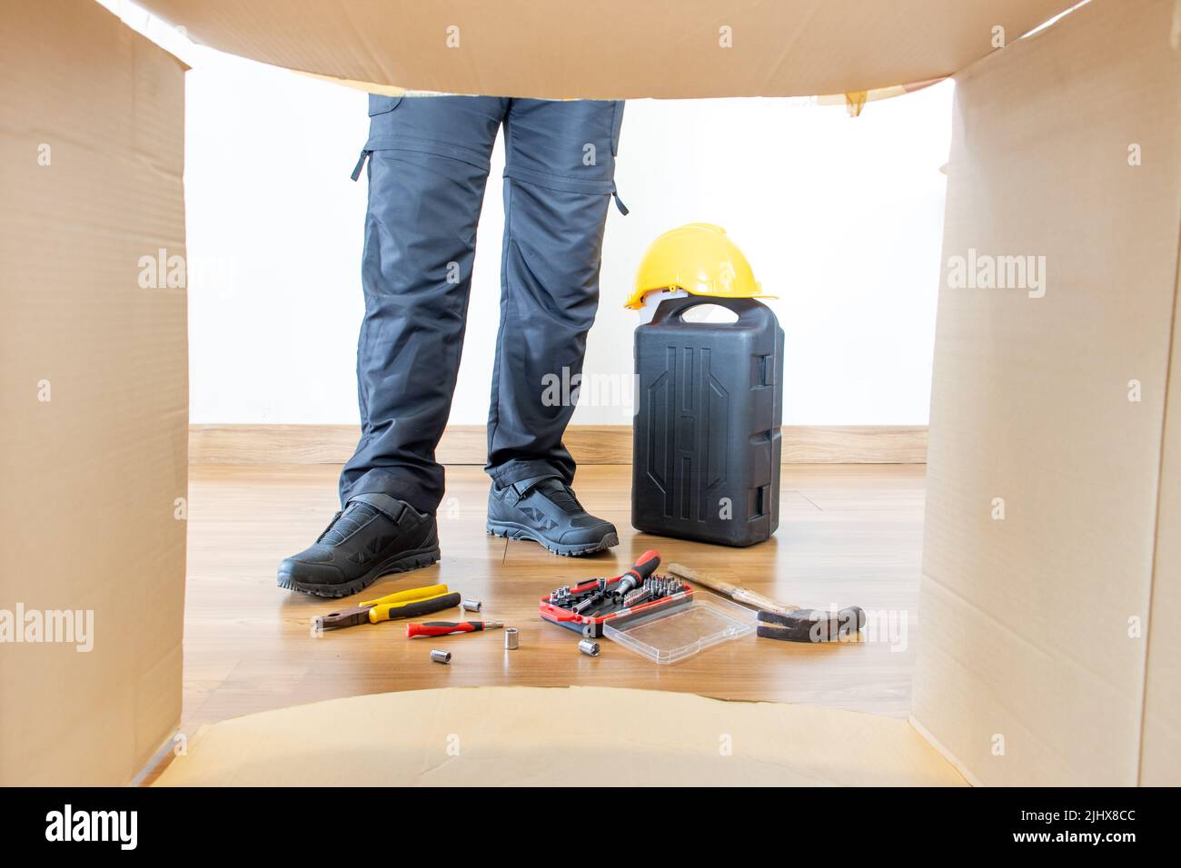 Beine eines Dienstmannes mit Werkzeugkasten an der offenen Papierkiste. Stockfoto