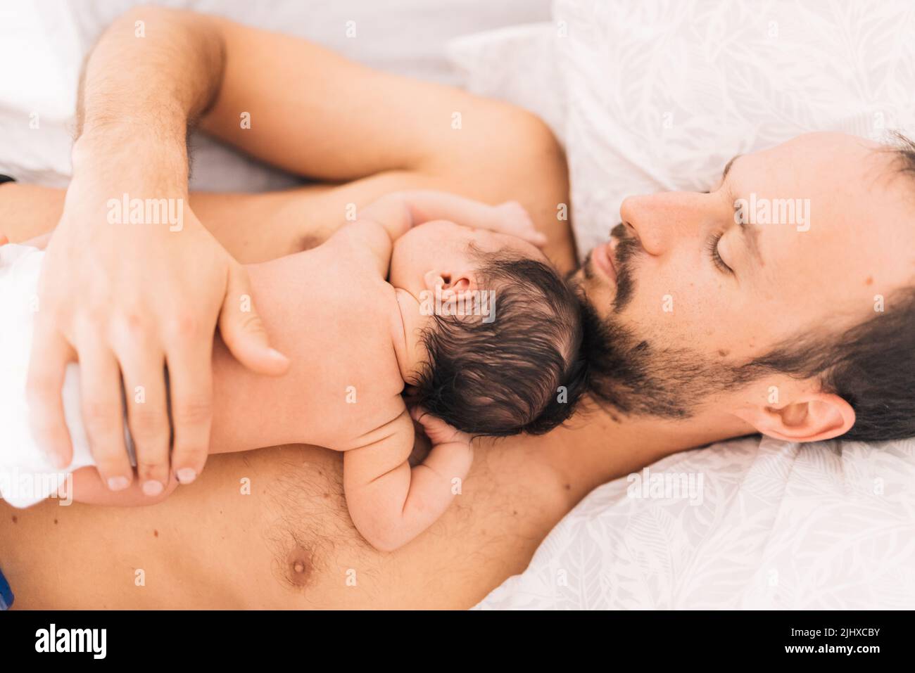 Junger glücklicher Vater mit seinem neugeborenen Sohn, der in einem zarten, intimen Vatermoment im Bett liegt Stockfoto