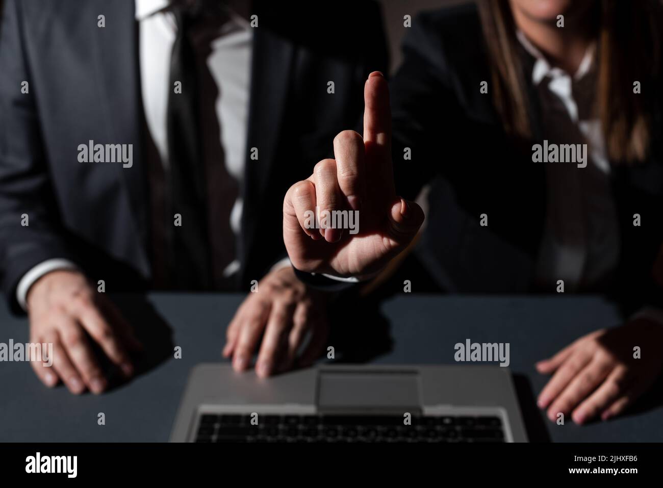 Sitzender Mann Auf Dem Schreibtisch Mit Lap Top Und Frau, Die Mit Einem Finger Auf Wichtige Botschaften Zeigt. Geschäftsfrau Präsentiert Krutialinformationen Mit Einer Hand Stockfoto