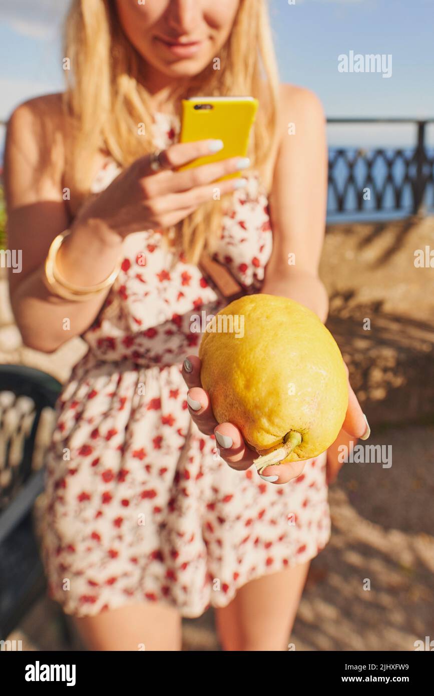 Sehen Sie sich die Größe dieser Zitrone an. Eine unkenntliche Frau, die allein steht und mit ihrem Mobiltelefon eine Zitrone in Italien fotografiert. Stockfoto