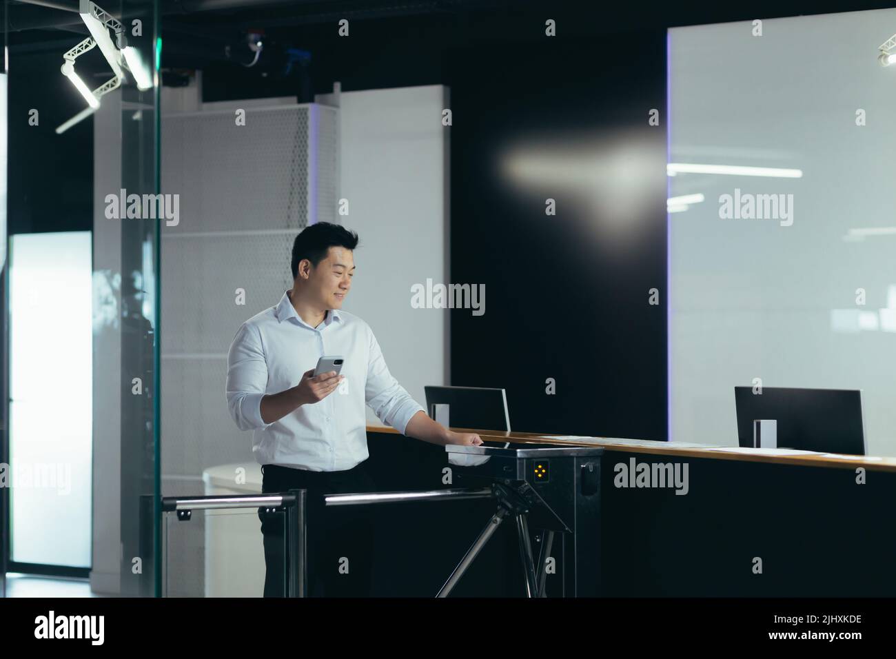 Ein asiatischer Arbeiter tritt durch die Tür ins Büro, öffnet das Schloss mit einer Plastikkarte, ein Geschäftsmann in einem Hemd mit einem Telefon Stockfoto