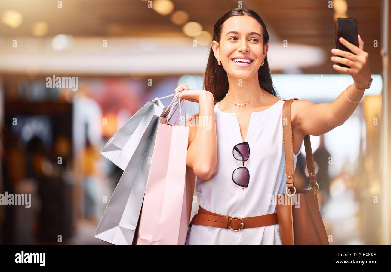 Glückliche junge Frau, die während eines Einkaufsbummel in einem Einkaufszentrum Selfies auf einem Handy macht. Eine Frau genießt beim Fotografieren nur die Verkaufstherapie Stockfoto