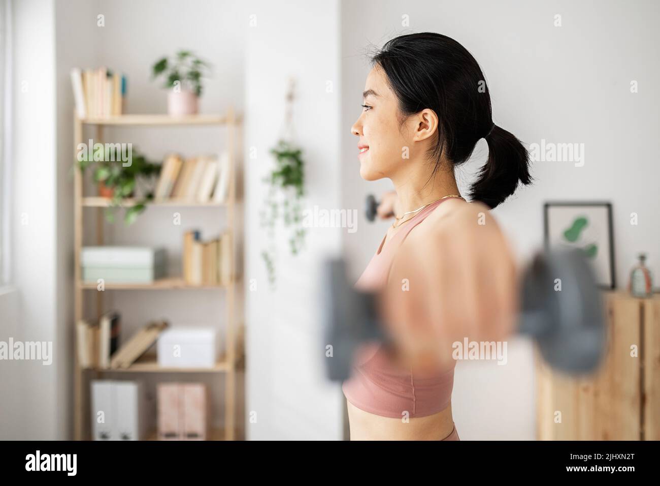 Junge Erwachsene asiatische Frau macht Übungen mit Hanteln im Wohnzimmer Stockfoto