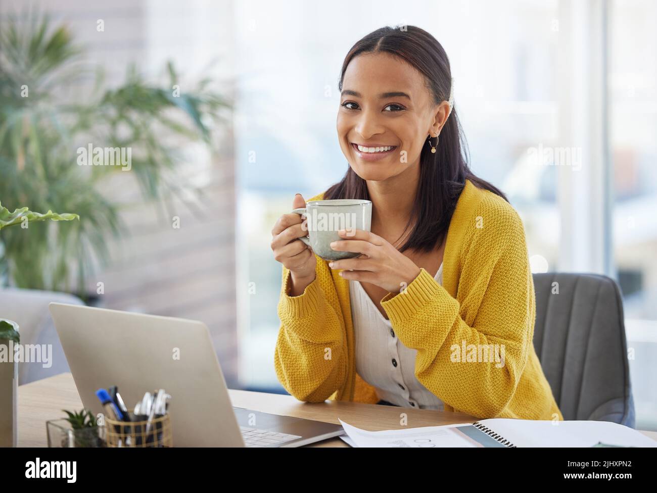 Kaffee vor der Arbeit. Eine junge Geschäftsfrau trinkt Kaffee in einem modernen Büro bei der Arbeit. Stockfoto