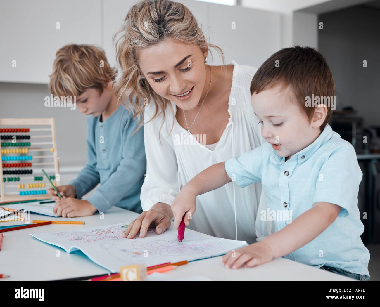 Alleinerziehende Mutter, die kleine Söhne während des Homeschool-Unterrichts zu Hause unterrichtet. Autistische niedliche kleine kaukasische Jungen lernen während ihrer Zeit lesen und schreiben Stockfoto