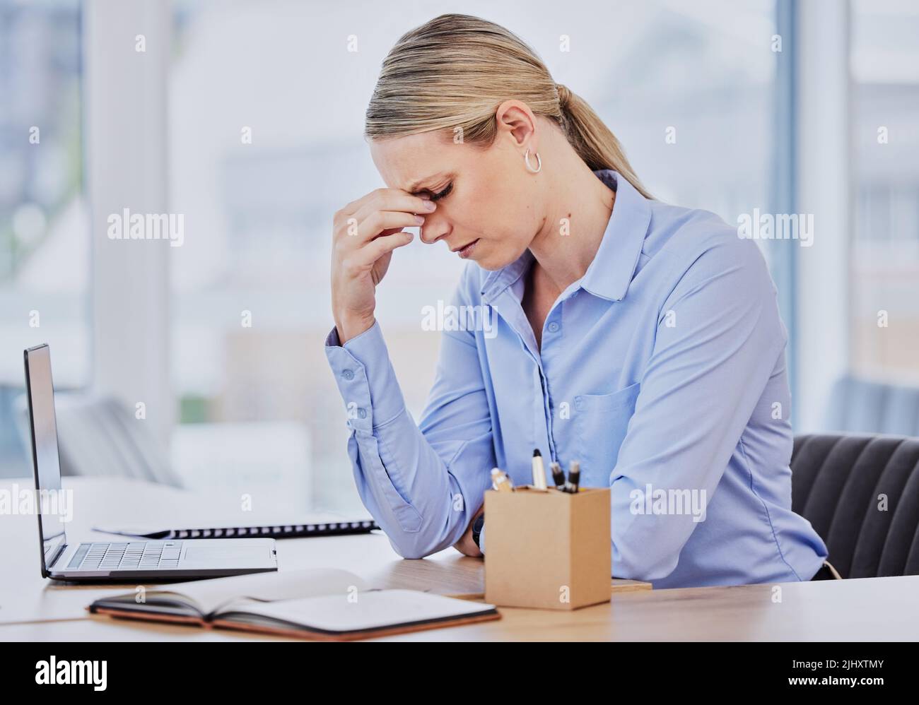Junge frustrierte kaukasische Geschäftsfrau, die am Schreibtisch arbeitet und unter chronischen Kopfschmerzen leidet, während sie vor dem Laptop sitzt. Weiblich Stockfoto