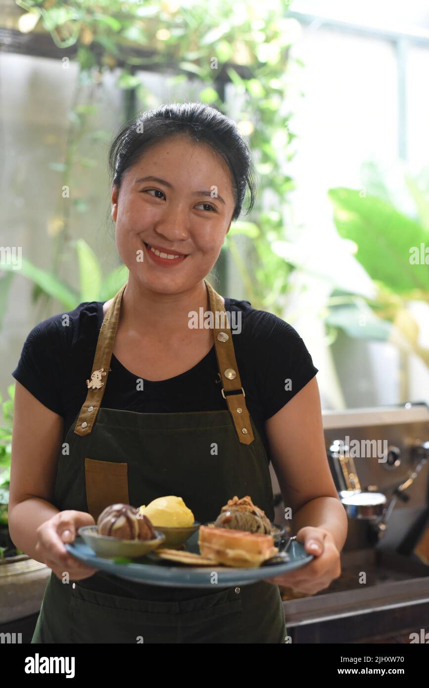 Vietnamesisches Mädchen, das in einem Café hausgemachtes Eis mit Waffeln serviert Stockfoto