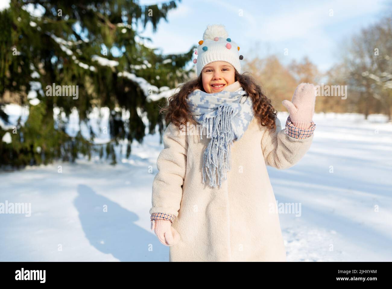 Glückliches kleines Mädchen winkt im Winter mit der Hand im Freien Stockfoto