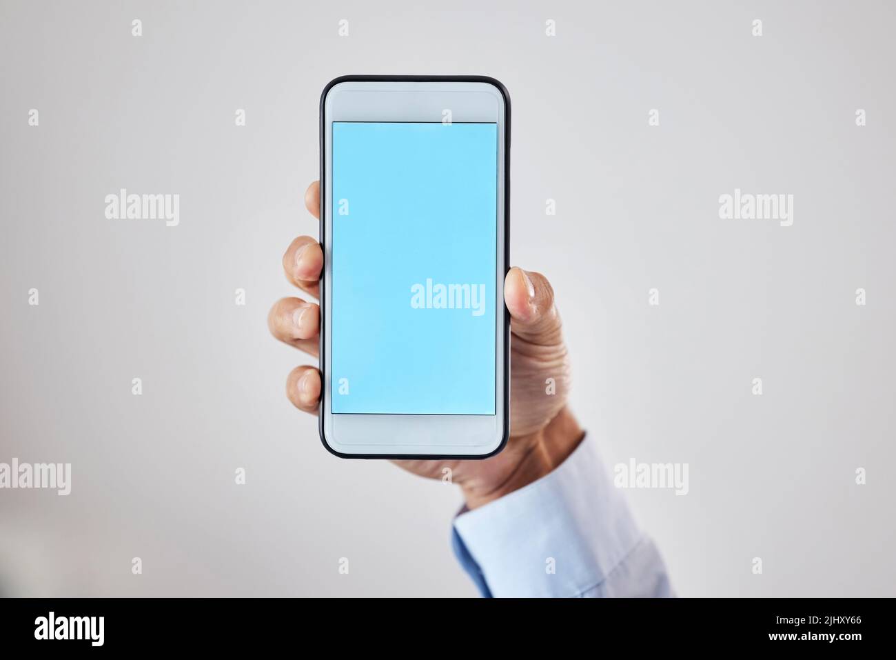 Nahaufnahme eines Mannes, der ein Mobiltelefon mit blauem leeren Bildschirm in der Hand vor grauem Studiohintergrund hält. Platz für Website- oder Mobile-App-Design. Mobiltelefon Stockfoto