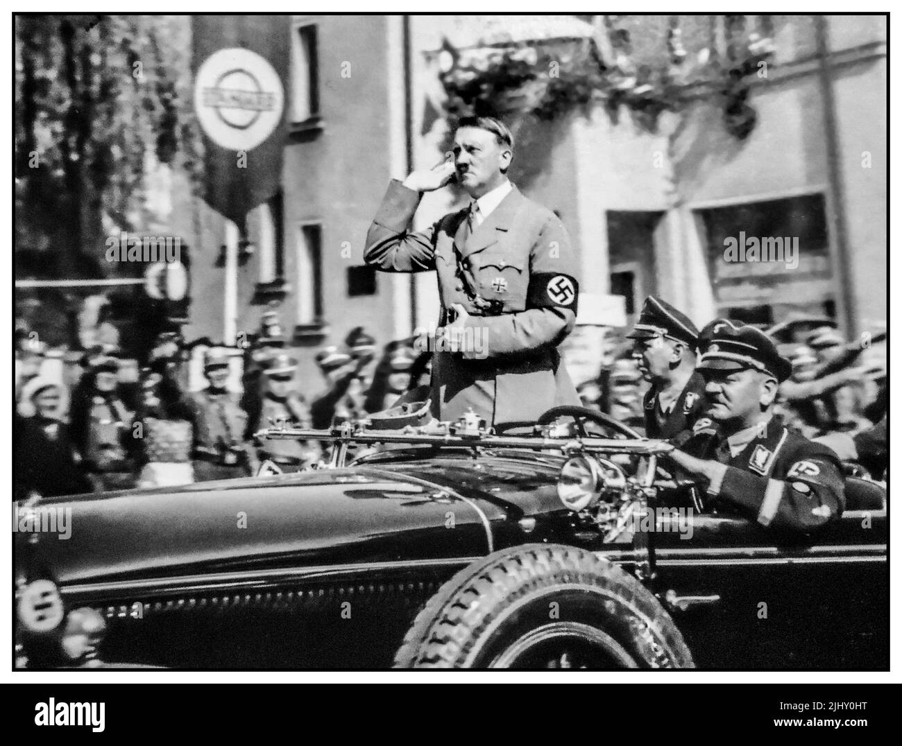 Adolf Hitler steht in seinem offenen Mercedes-Motorwagen, grüßt seine Truppen und begrüßt Menschenmengen, indem Heil Hitler Nazi-Deutschland 1930s begrüßt Stockfoto