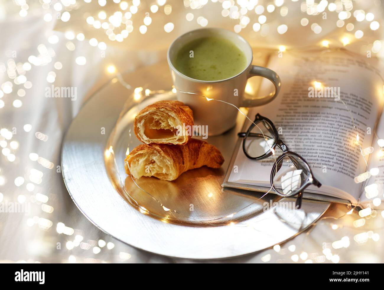 Croissants, Matcha-Tee, Buch und Gläser im Bett Stockfoto