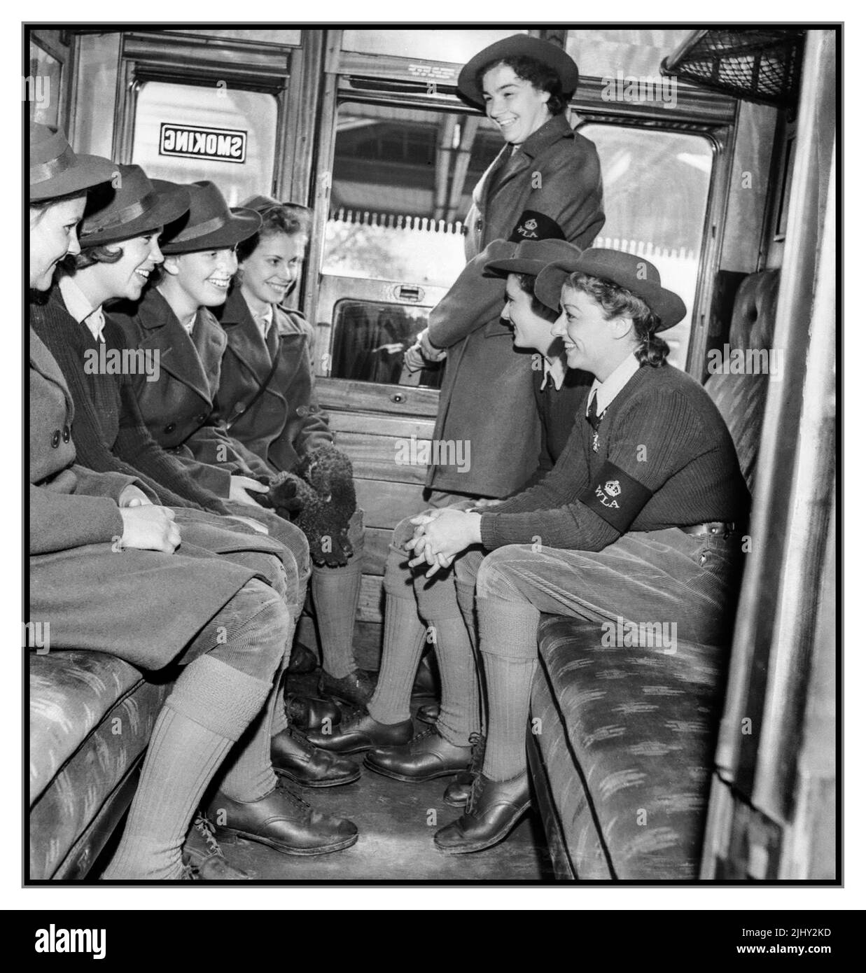 WW2 Frauen-Landarmee-Mädchen in einem Eisenbahnwaggon, die ihre WLA-Armbänder auf dem Weg zu ihren jeweiligen Landgütern tragen. Battle of the Land - die landwirtschaftliche Arbeit der Women's Land Army an der britischen Heimatfront, die frisches Gemüse für das Vereinigte Königreich liefert, 1942. Weltkrieg 2. Weltkrieg WW2 Stockfoto