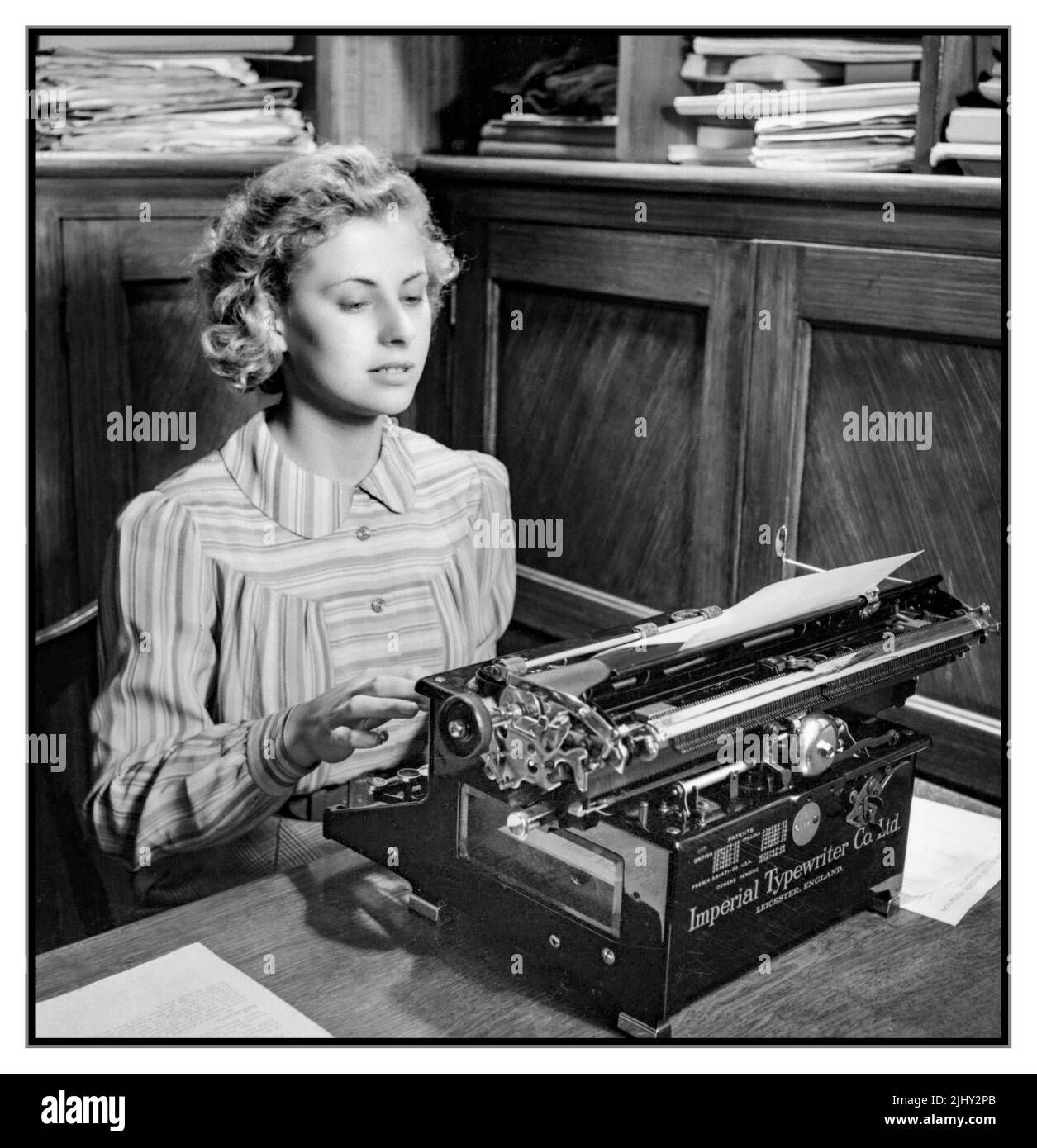 1940s Fashion Style Technology Büroverwaltung mit Schreibtischsprecherin, die Bericht/Brief auf einer kaiserlichen Schreibmaschine schreibt, mit traditionellen alten Büropapierregalen und Papierkram Stockfoto