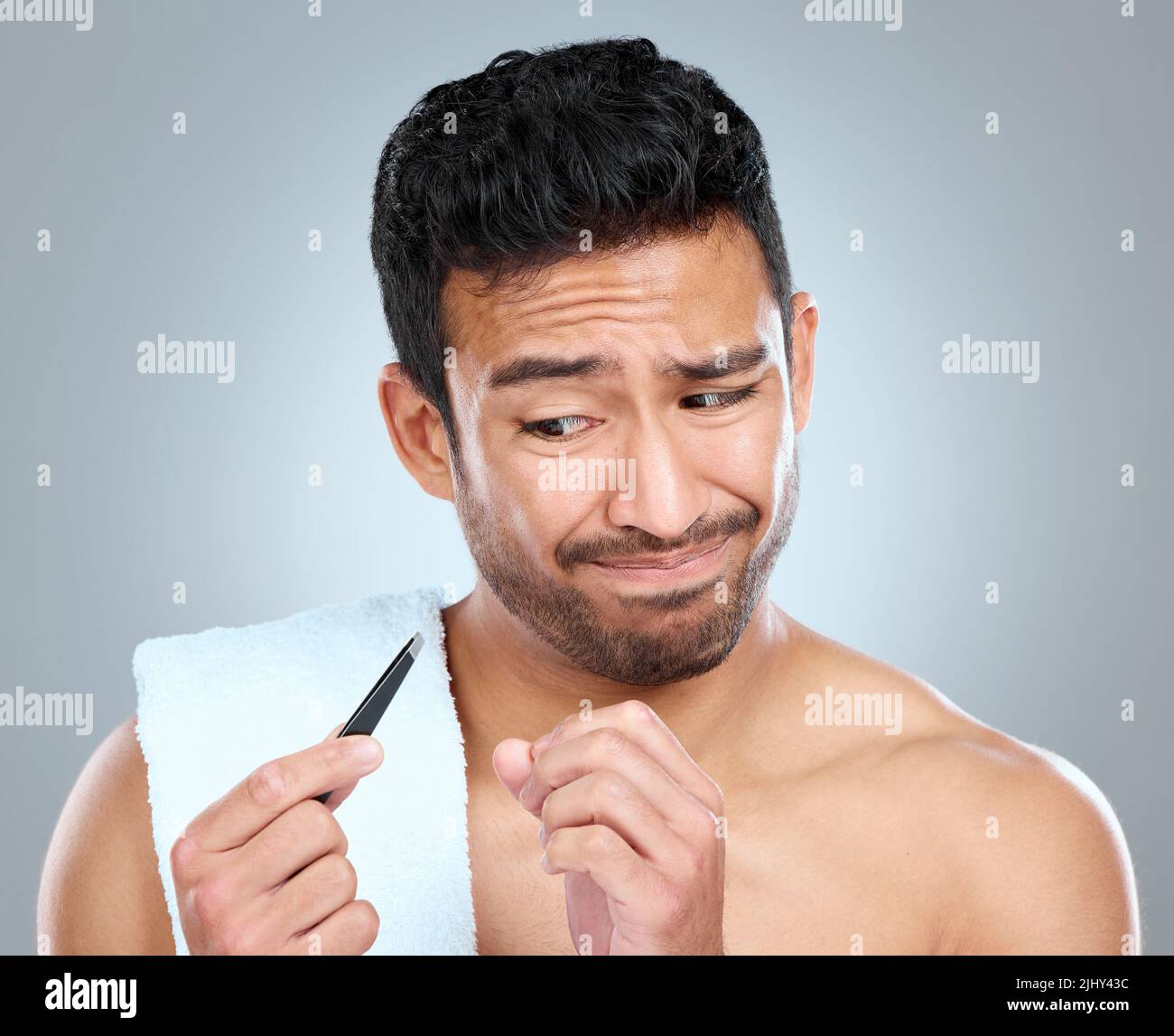 Ich bin mir nicht so sicher, ob ich das machen möchte. Ein Mann, der skeptisch über die Verwendung einer Pinzette schaut. Stockfoto