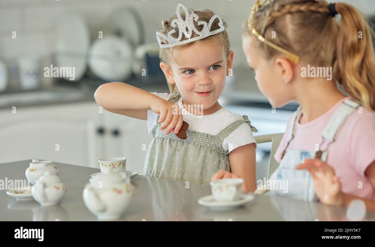Zwei kleine Mädchen mit einer Prinzessin Tee-Party zu Hause. Geschwisterfreunde tragen Tiaras, während sie mit dem Teeset spielen und in der Küche Kekse trinken Stockfoto