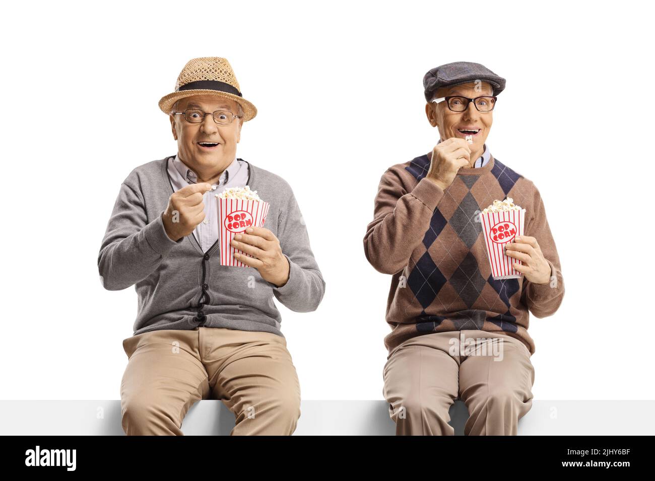 Ältere Männer, die auf einer Wand sitzen und Popcorn essen und auf weißem Hintergrund vor der Kamera lächeln Stockfoto