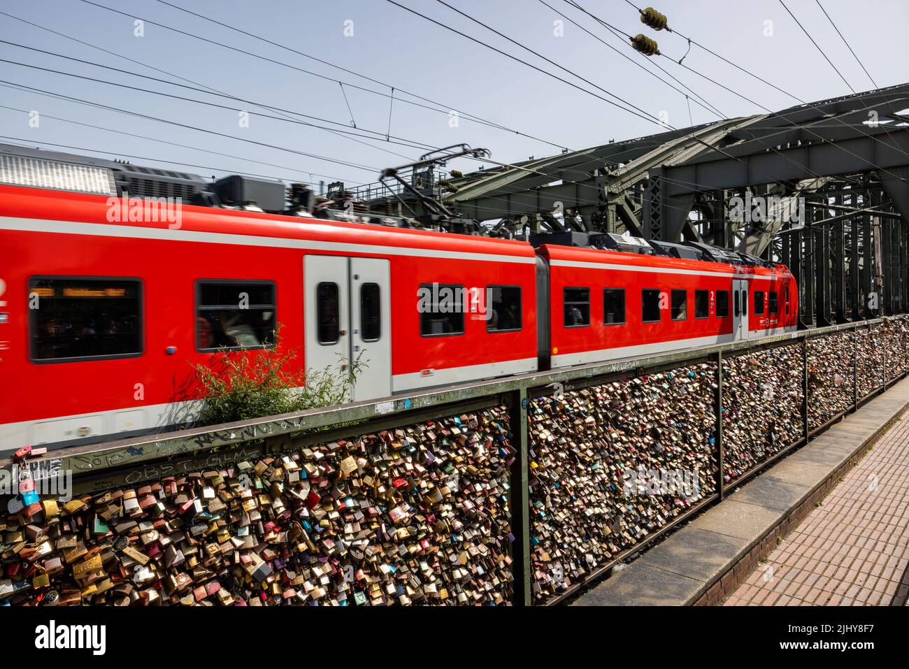 Vorhängeschlösser am Zaun der Hohenzollerneisenbahn-Brücke mit vorbeifahrenden Zug, Köln, Deutschland Stockfoto