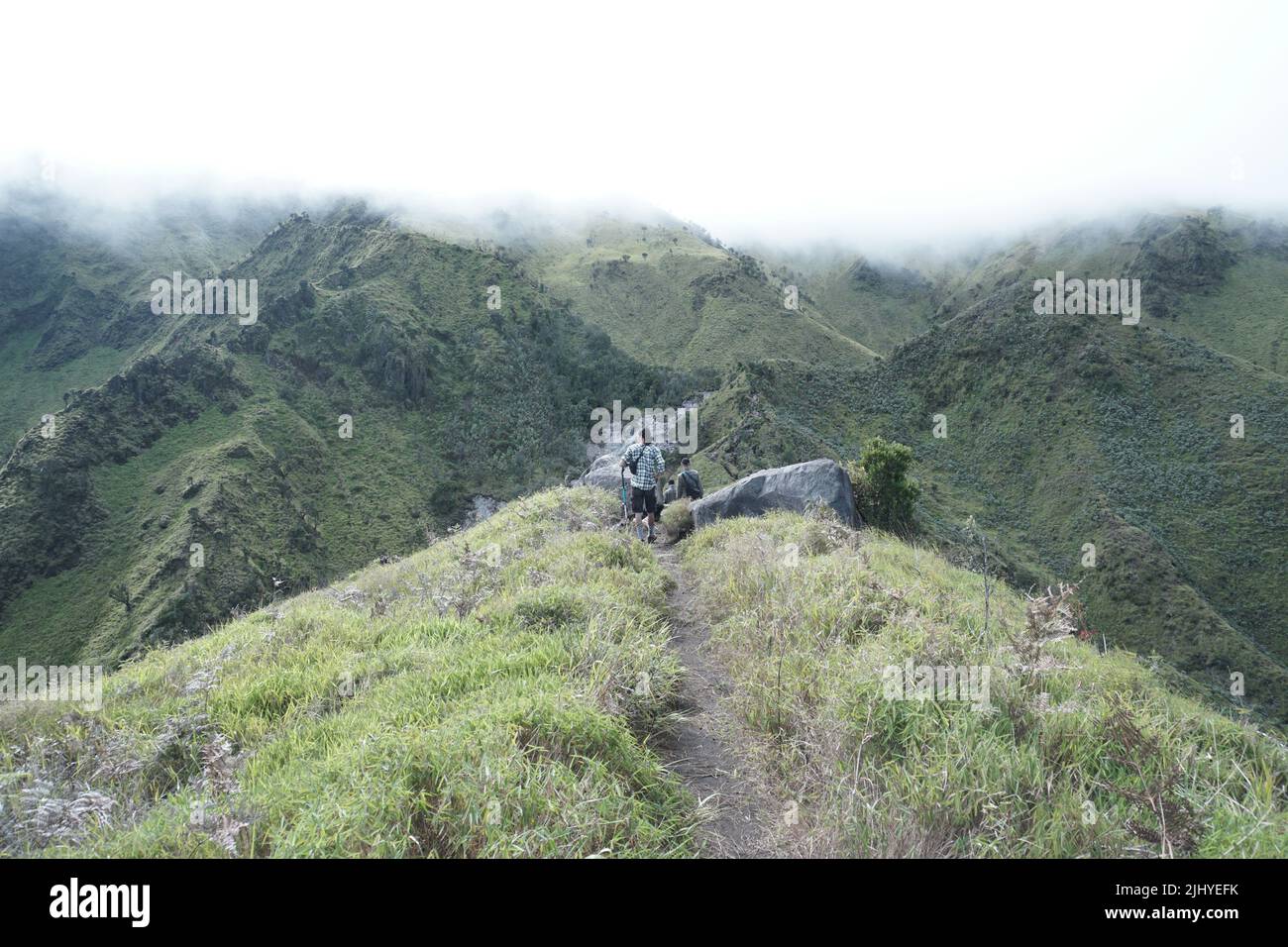 Langhaariger Junge im Hintergrund, in Wolken gehüllte grüne Berge, indonesische Stock-Fotografie Stockfoto