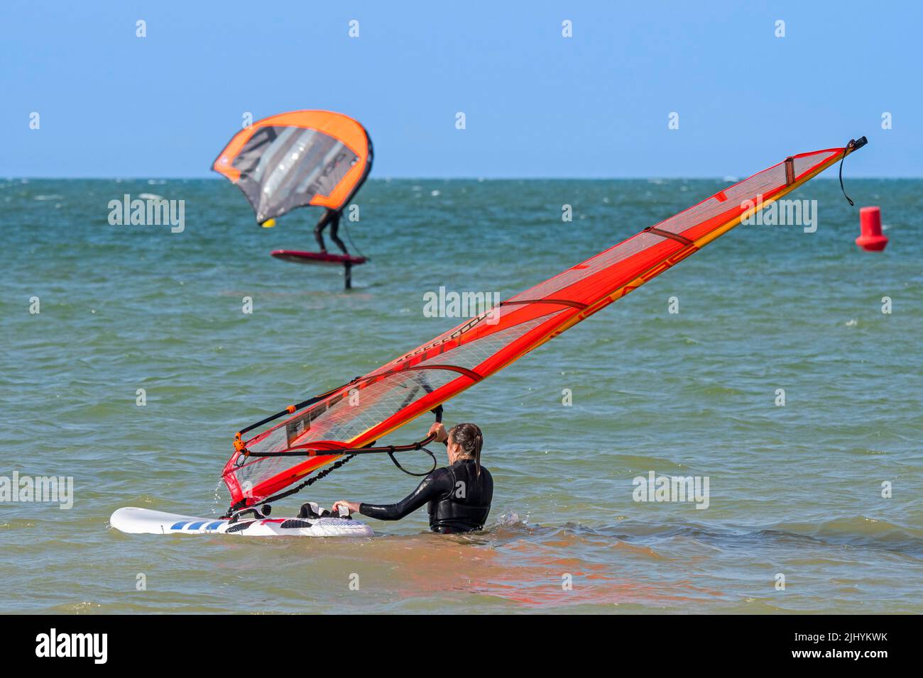 Windsurferin beim Einstieg ins Wasser und Wingboarderin / Wing Boarderin auf Foilboard / Hydrofoil Board Surfen mit aufblasbarem Flügel an der Nordsee Stockfoto