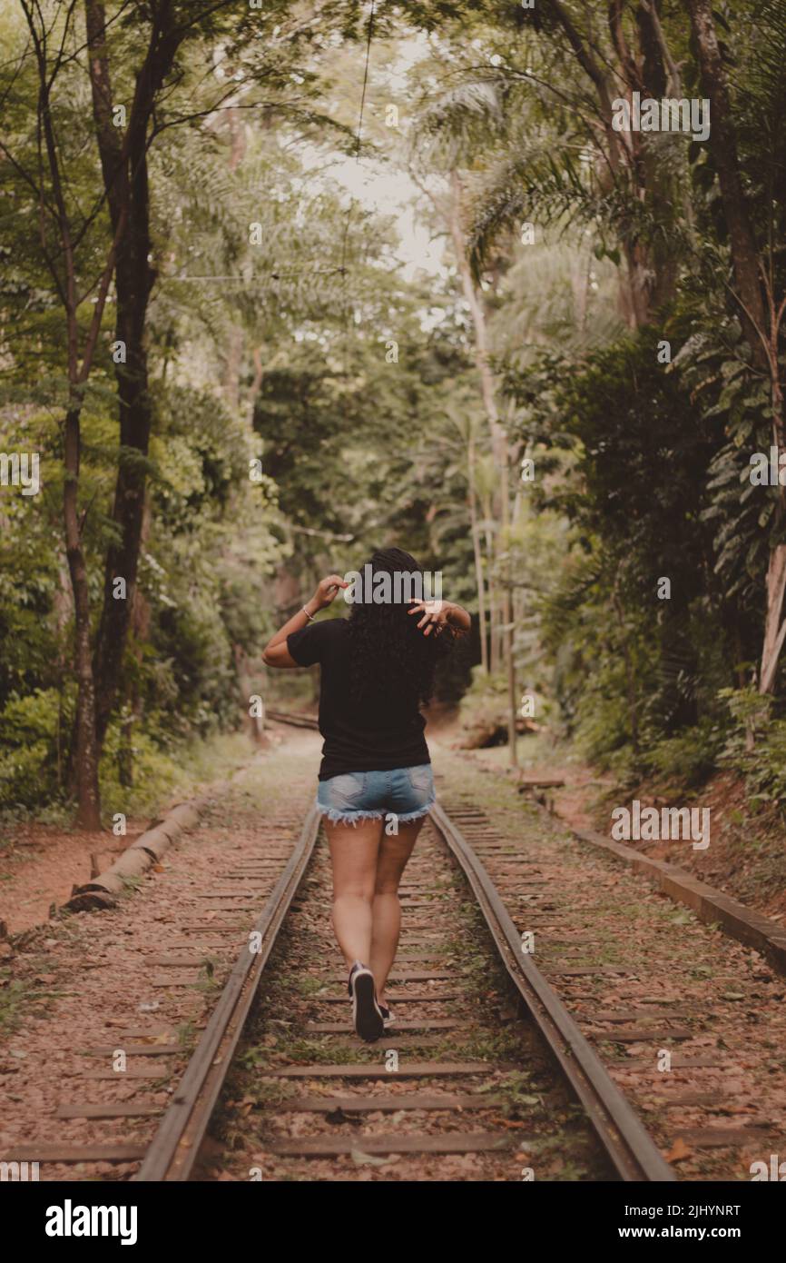 Rückansicht einer jungen Frau, die alleine auf Schienen läuft und mit Haaren herumfiddelt Stockfoto