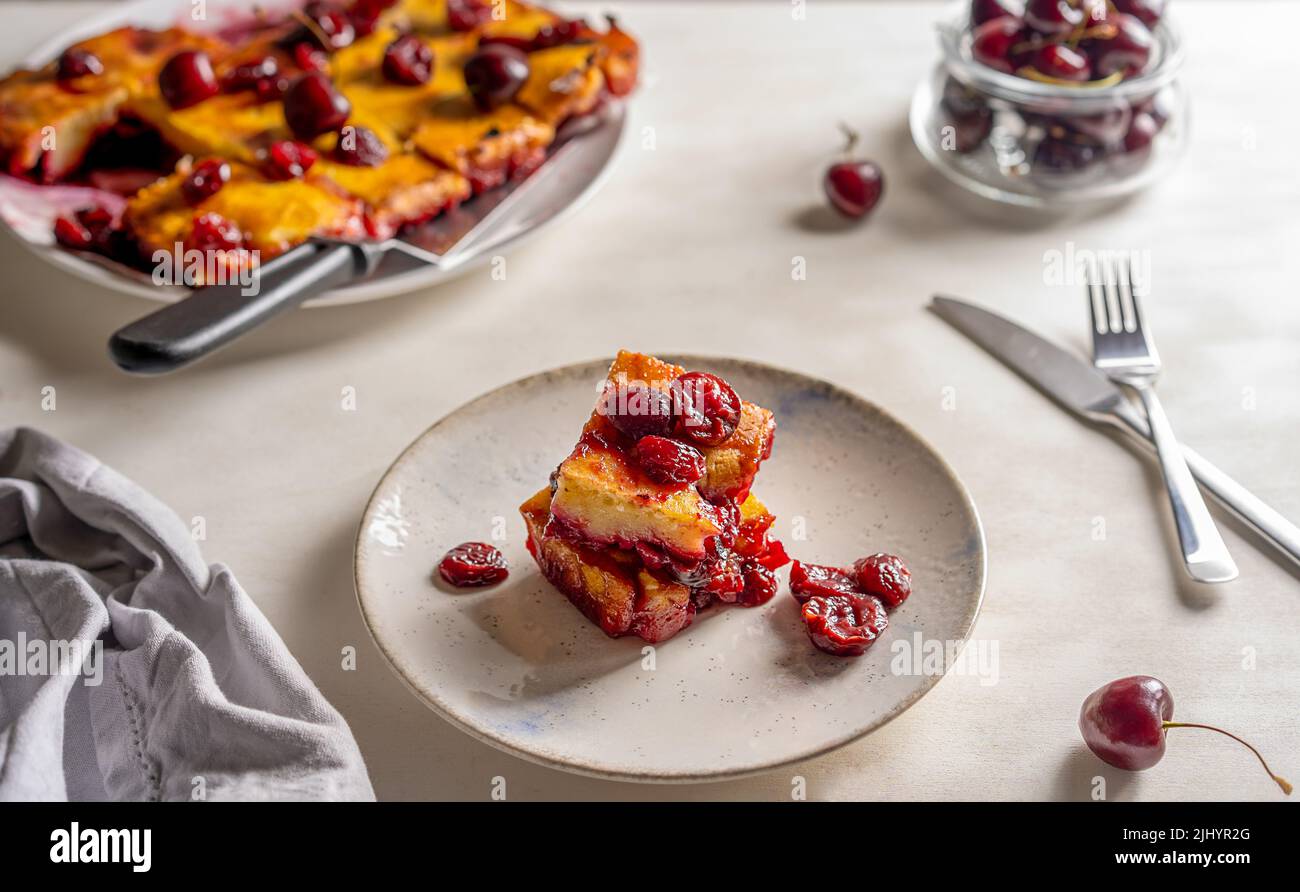 Süßer Kirschkuchen oder roter Brownie-Kuchen. Ein Stück Kuchen auf dem Teller, ganzer Kuchen und rohe Kirschen im Rücken Stockfoto