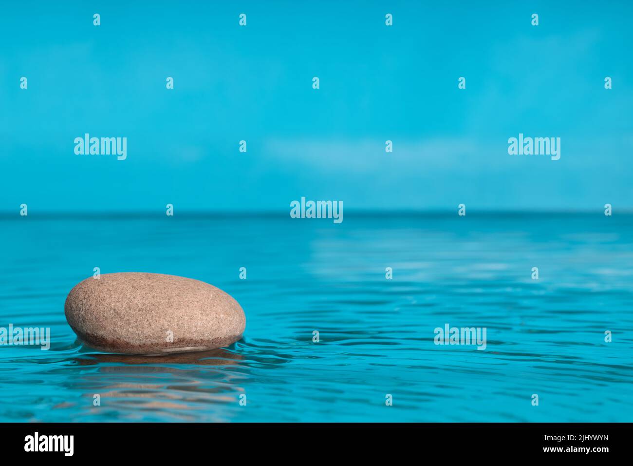 Minimalistische Komposition im Zen-Stil. Stein im Wasser mit Platz für Text. Blaue Farbe, Kopierraum . Stockfoto