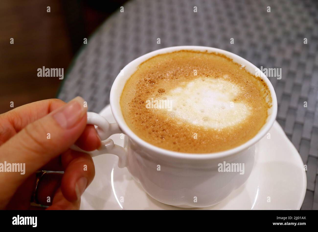 Hand hält eine Tasse Cappuccino-Kaffee mit herzförmiger Latte-Kunst Stockfoto