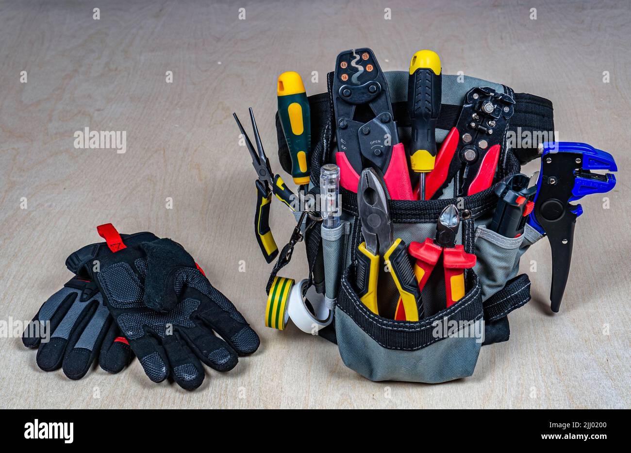 Elektriker-Tasche mit professionellen Elektrowerkzeugen und Handschuhen. Zangen, Drahtschneider, Abisolierer, Schraubendreher, Tester, Crimpzange. Sperrholzrücken Stockfoto
