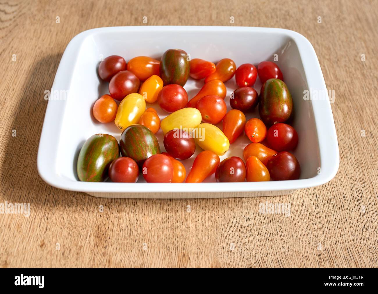 Viele Kirschtomaten in einer Schüssel. Viel buntes Bio-Tomatengemüse für eine gesunde vegetarische Platte. Bunte kleine leckere Frucht, perfekt Stockfoto