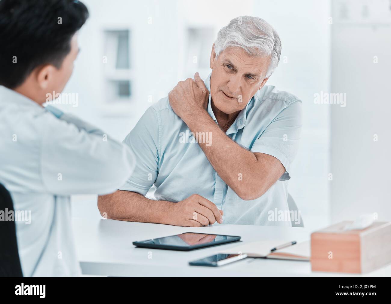 Yup, genau hier. Ein reifer Mann, der mit seinem Arzt sitzt und sich während einer Konsultation über eine schmerzende Schulter beschwert. Stockfoto