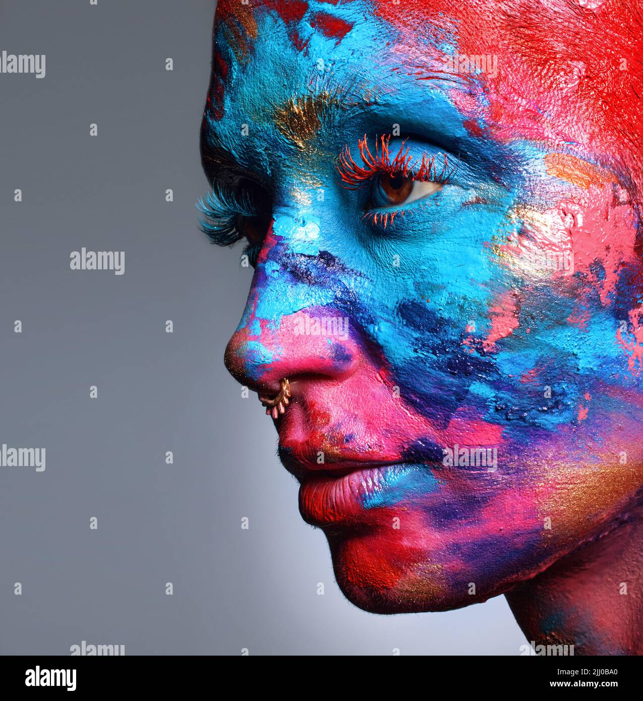 Kunst ist das, was man sieht und fühlt. Eine attraktive junge Frau posiert allein im Studio mit Farbe auf ihrem Gesicht. Stockfoto