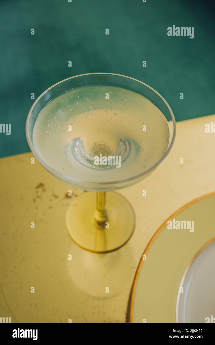 Prickelndes Wasser, Blasen, Champagner in gelbem Stengelglas auf goldenem Tisch, blaugrün Stockfoto