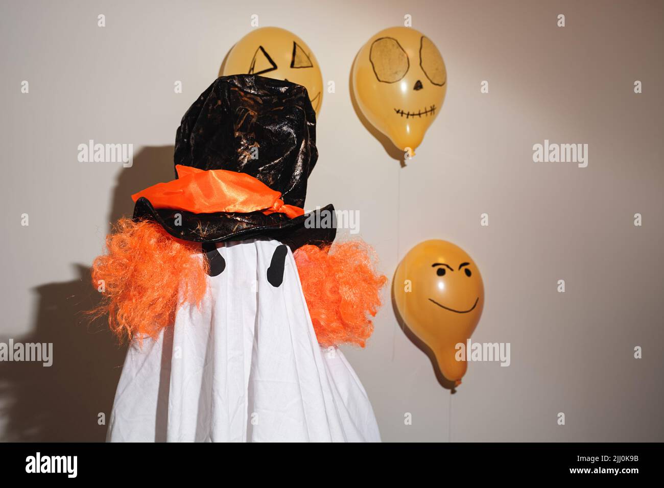 Frohe Halloween. Weißer Geist in einem selbstgemachten Kostüm aus einem Heimtuch und bemalt mit orangefarbenen Kugeln an der Wand. Festliches Design, Partykonzept. Feier zum Allerheiligen. Stockfoto