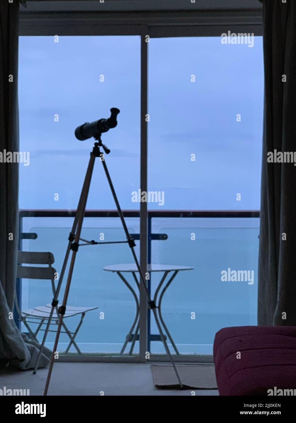 Ein Fernglas auf Stativen vor dem Glasfenster mit einer Meereslandschaft Stockfoto