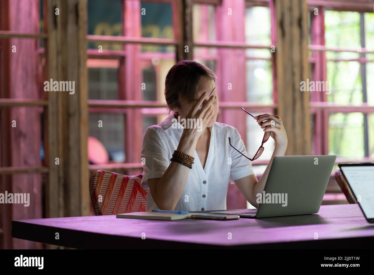Müde weibliche Angestellte, die die Brille auszieht und die Augen reibt und lange Stunden vor dem Laptop-Bildschirm verbringt Stockfoto