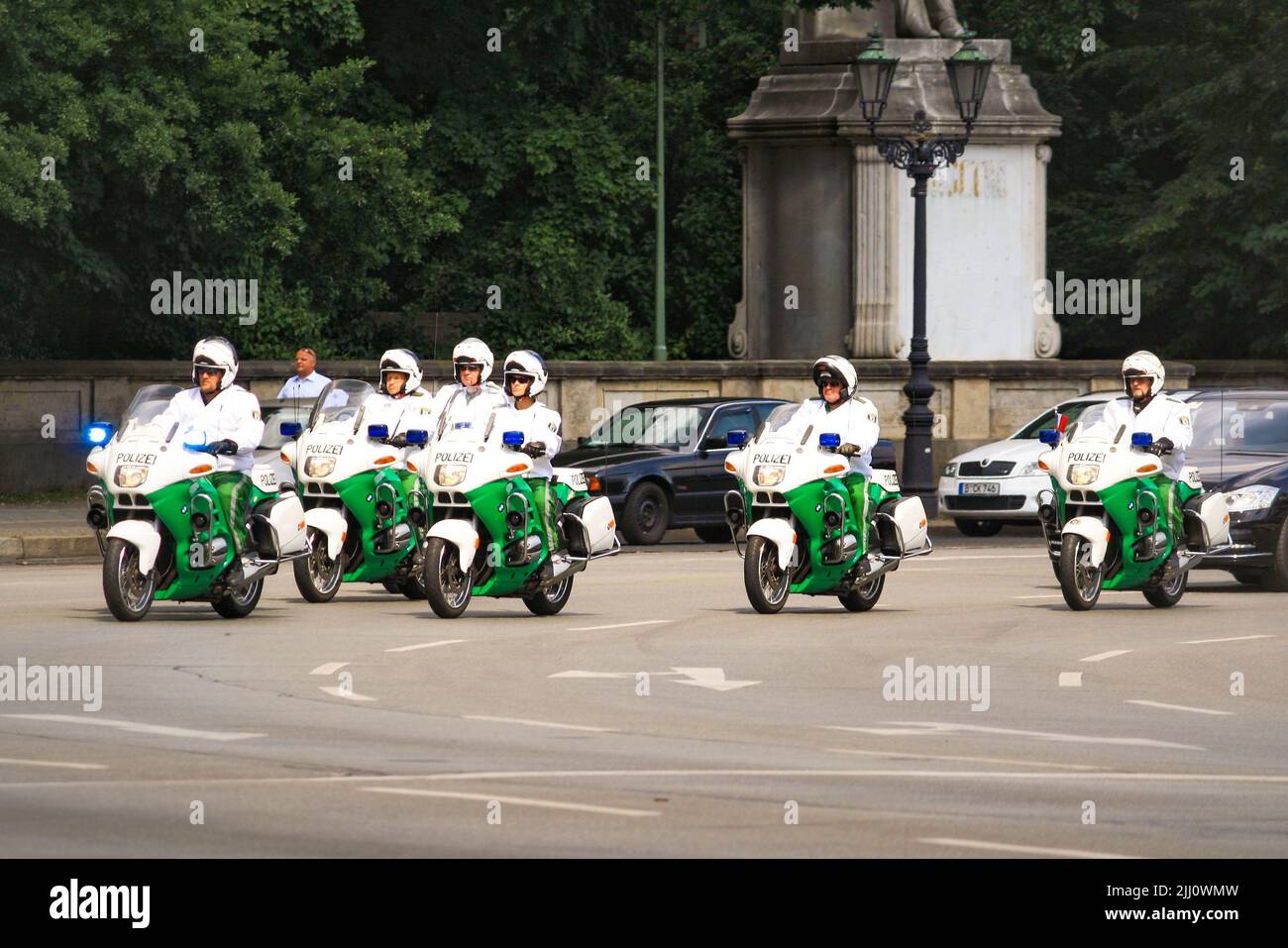 Blick auf Polizisten mit Helm auf grün-weißem Motorrad-Fahrt im VIP-Autokonvoi an der Siegessäule, Tiergarten im Sommer mit Bäumen im Hintergrund. Stockfoto