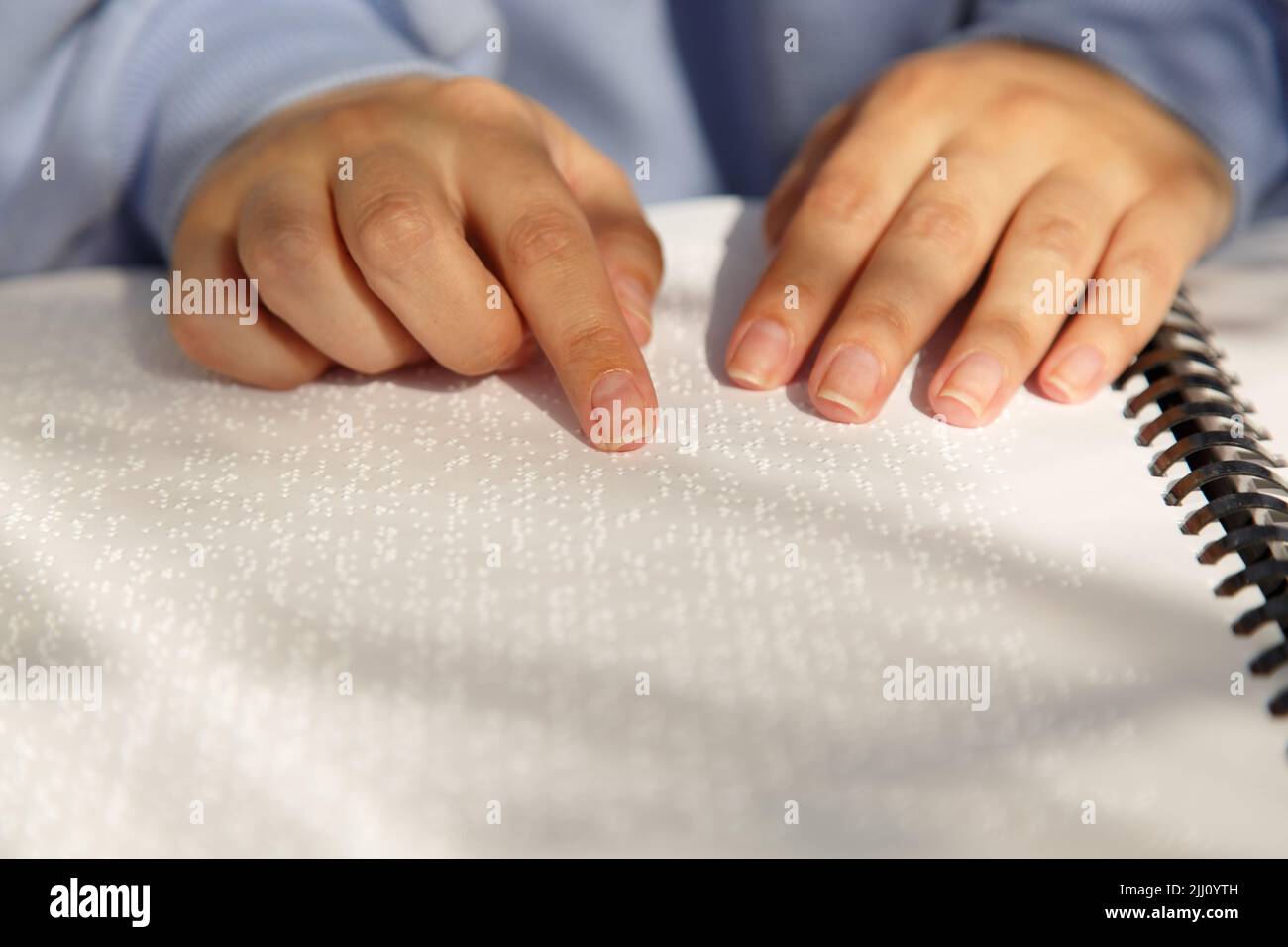 Damenhänden mit violetten Ärmeln auf Buch in Louis Braille Schrift Stockfoto