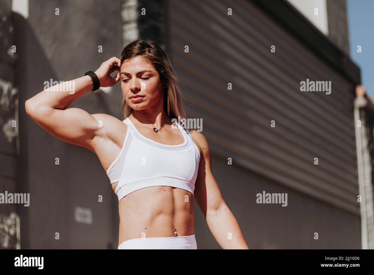 Muskulöse Frau, die nach einem Training in Weiß in Sonnenschein sitzt Stockfoto