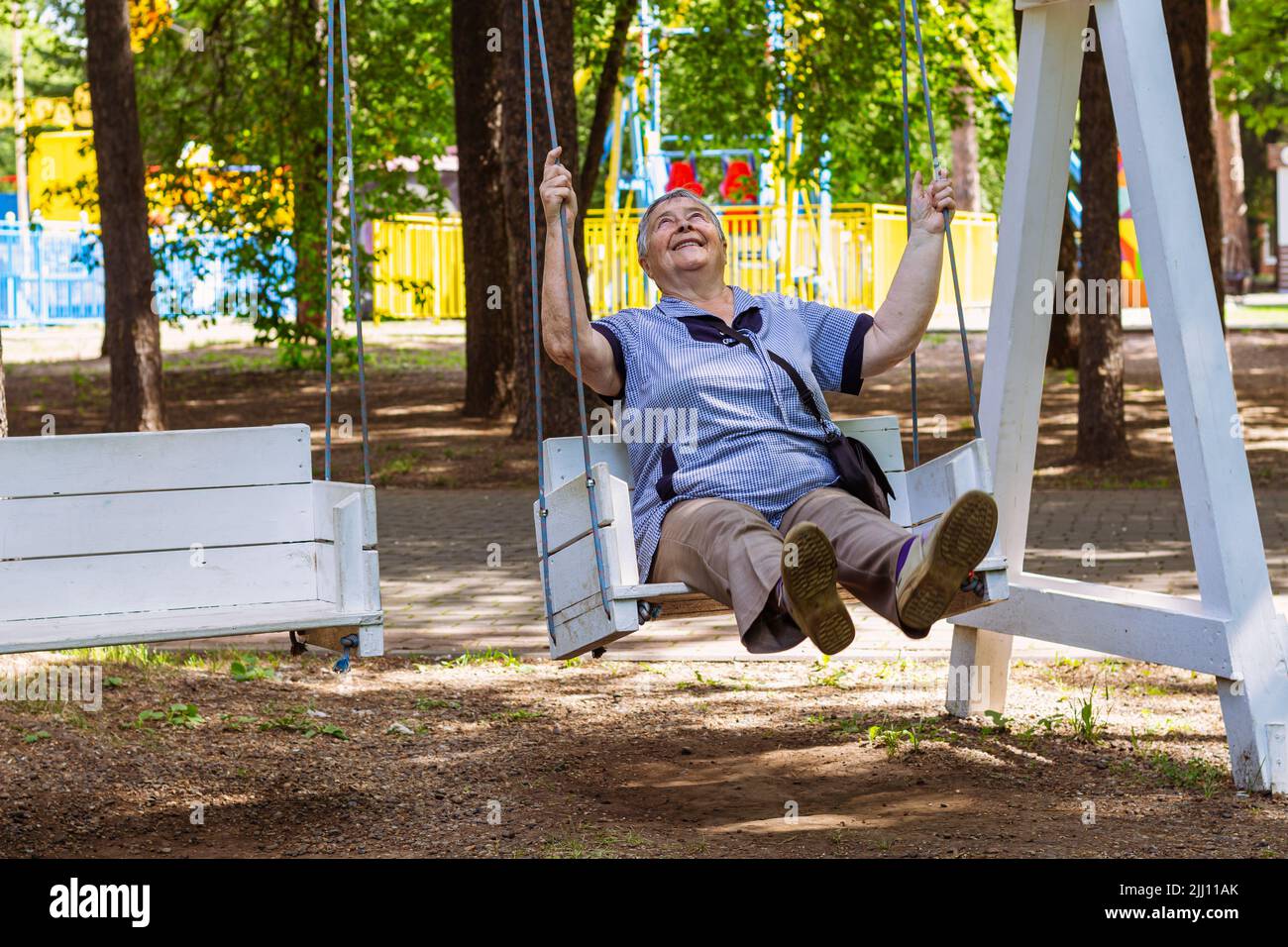 Verspielte und glückliche ältere Frau genießen bei Schaukel im Freien in Park oder Garten entspannt, fröhlich aktiven Ruhestand und Entspannungskonzept. Großeltern Tag Stockfoto
