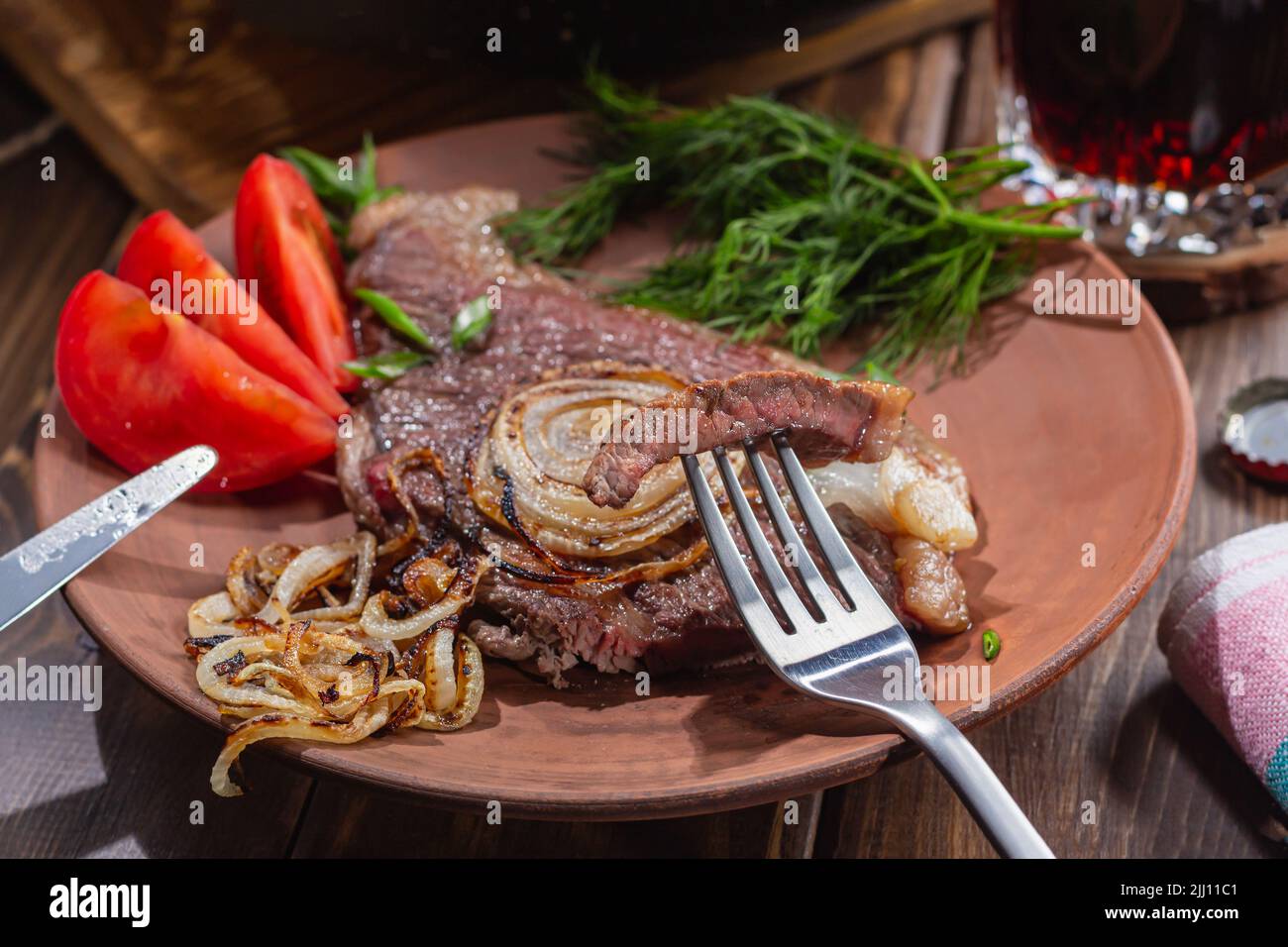 Köstliches herzhaftes Abendessen, zubereitet von einem Mann. Konzentrieren Sie sich auf ein Stück marmoriertes Rindersteak auf der Gabel. Fleisch, Bier, Tomaten und Dill für eine komplette Mahlzeit. Stockfoto