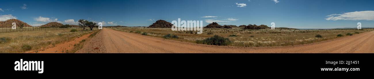 Ein Panoramabild einer Schotterstraße mitten in Namibia. Cairns mit großen Felsbrocken in der Mitte, blauer Himmel mit verstreuten weißen Wolken. Stockfoto