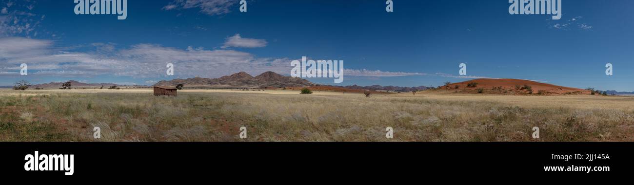 Ein Panoramafoto von Hügeln und Bergen in Zentral-Namibia bei Sossusvlei. Erste rote Dünen der Namib-Wüste sichtbar. Blauer Himmel mit Wolken. Stockfoto