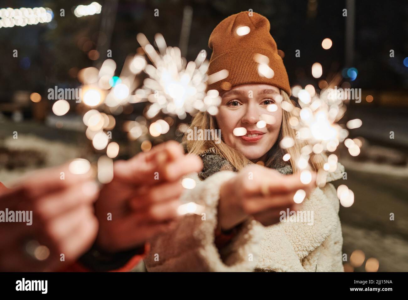Horizontale, mittlere Nahaufnahme der jungen Frau und ihres Freundes, die am Winterabend draußen mit brennenden Wunderkerzen stehen Stockfoto