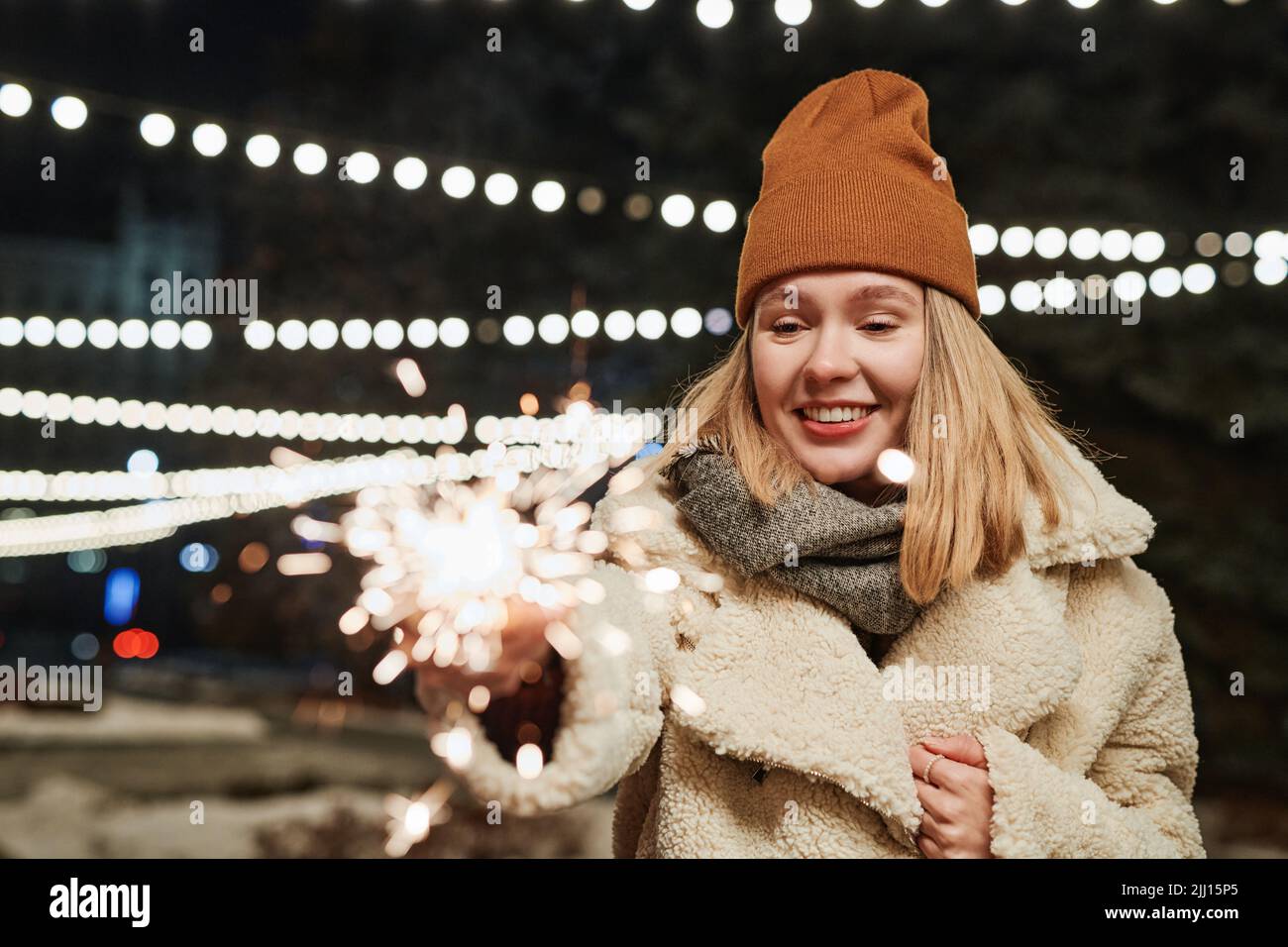 Horizontale Porträtaufnahme einer jungen kaukasischen Frau, die am Winterabend im Freien steht und brennenden Funker hält Stockfoto