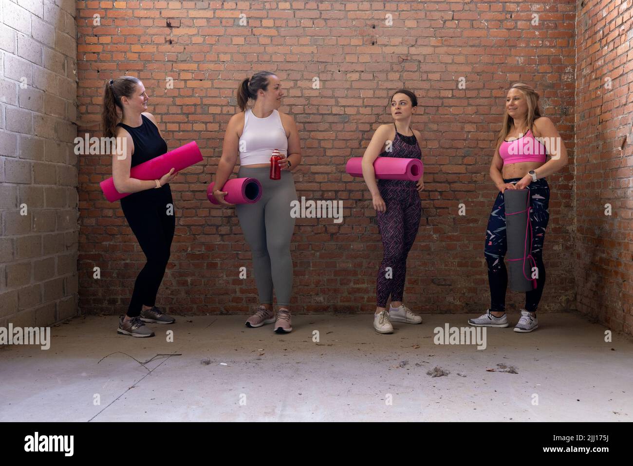 Eine vielfältige Gruppe junger, attraktiver, sportlicher Frauen unterschiedlicher Körperformen versammelten sich und unterhielten sich während des Wartens im Fitnessstudio. Industrielle Backsteinmauer Hintergrund. Hochwertige Fotos Stockfoto