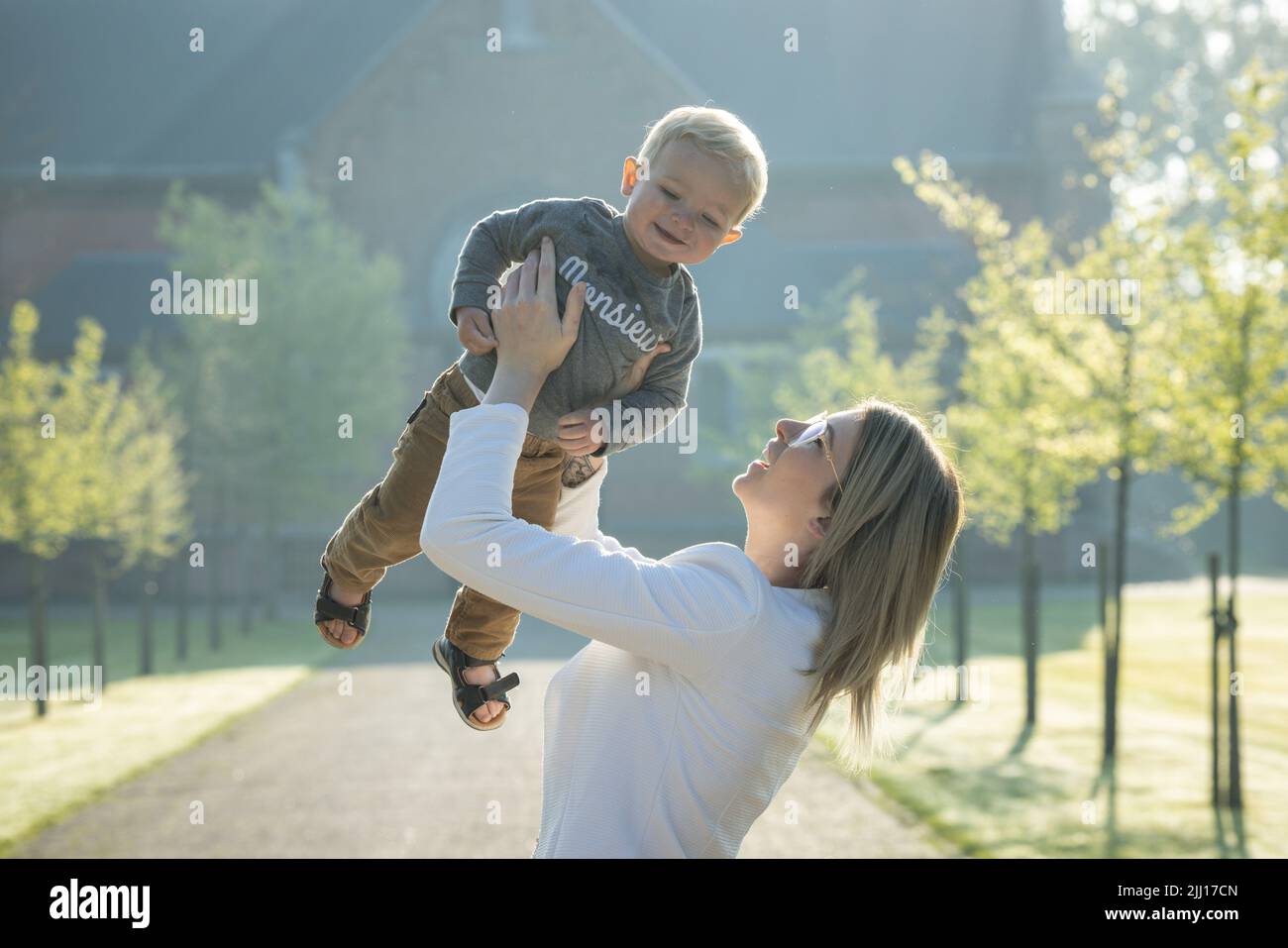 Eine junge und glückliche Mutter und ein Kind, spielend, stehen inmitten eines Parks in den Strahlen der aufgehenden Morgensonne. Hochwertige Fotos Stockfoto