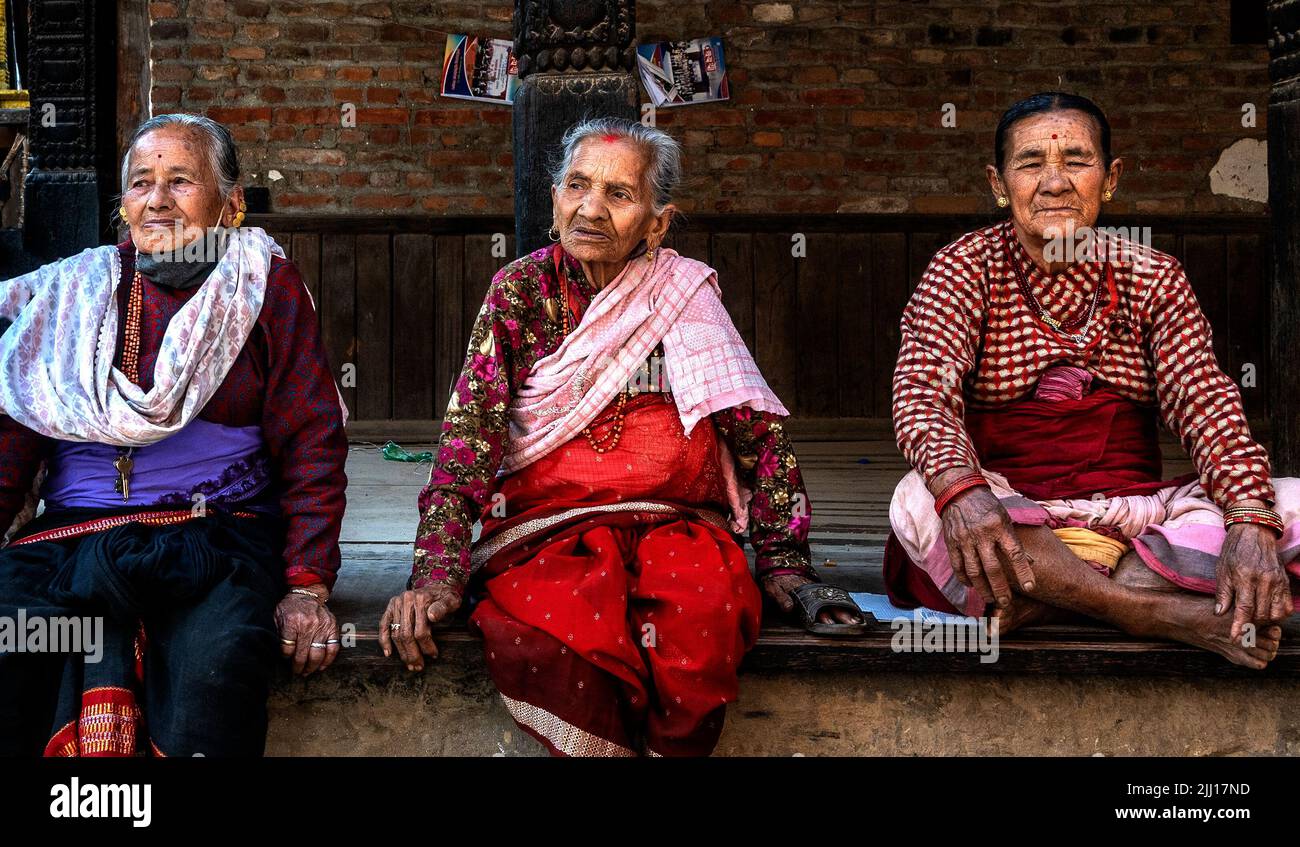 Alte nepalesische Frauen, die in einheimischen traditionellen Kleidern gekleidet sind, sitzen auf einer Steinterrasse in der Stadt Bhaktapur in der Nähe von Kathmandu in Nepal, Asien. Stockfoto